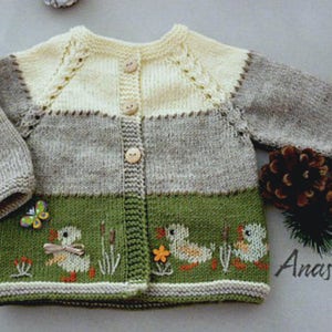 May include: A knitted baby cardigan with a beige, gray, and green color scheme. The cardigan has a button closure and features embroidered ducks and a butterfly.