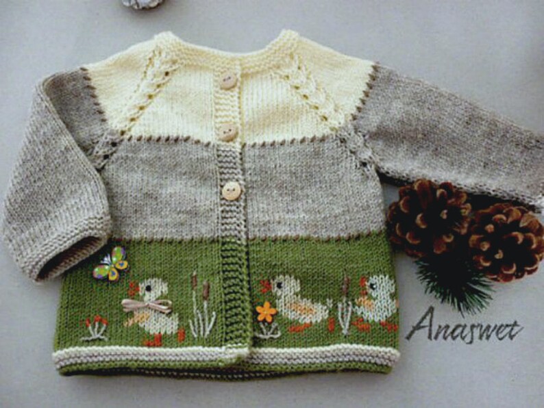 May include: A knitted baby cardigan with a beige, gray, and green color scheme. The cardigan has a button closure and features embroidered ducks and a butterfly.