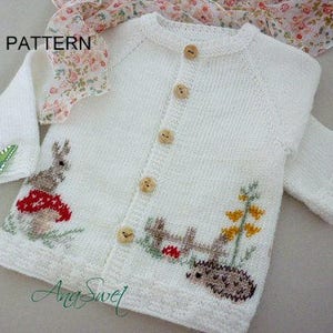 May include: White knitted baby cardigan featuring a bunny, mushroom, hedgehog, and fence design. The cardigan has a button fastening and is decorated with a green butterfly on one sleeve. The text "PATTERN" is visible in the top left corner of the image.