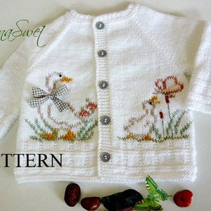 Puede incluir: Cárdigan de bebé de punto blanco con un encantador diseño de ganso. El cárdigan presenta un ganso con un lazo y un ganso más pequeño con flores. La palabra "PATTERN" está impresa en la parte inferior. El cárdigan tiene tres botones.