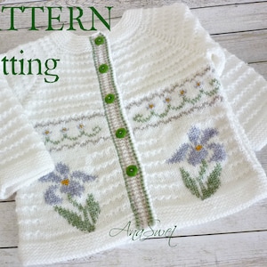 May include: White knitted cardigan with a green and grey floral pattern. The cardigan has a button closure and is made with a soft, textured yarn.