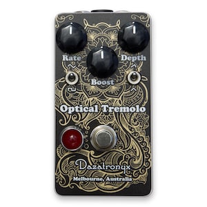Op de afbeelding: Zwart Optical Tremolo gitaareffectpedaal met gouden filigraan ontwerp. Voorzien van drie zwarte knoppen met de labels Rate, Boost en Depth, en een rode voetschakelaar. De tekst "Optical Tremolo" en "Dazatronyx Melbourne, Australia" zijn zichtbaar.