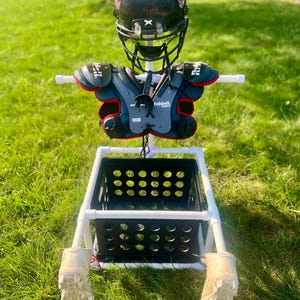 May include: White PVC pipe stand with a black plastic crate, a black football helmet with a red and white logo, and black and red shoulder pads. The helmet and shoulder pads are hanging on the stand.