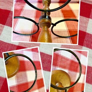 K&ouml;nnte beinhalten: Ein Weinhalter aus Holz mit einem Design aus dunklen Metallringen. Der Halter hat eine hellbraune Oberfl&auml;che und ist f&uuml;r mehrere Flaschen ausgelegt. Der Hintergrund ist ein rot-wei&szlig; kariertes Muster.