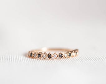 May include: A rose gold ring featuring a series of alternating black and clear stones set within individual diamond-shaped metal frames. The band has a geometric, repeating pattern that spans the visible portion of the circular jewelry piece.