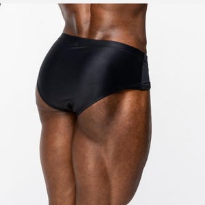 May include: Solid black swim briefs featuring a smooth, form-fitting fabric construction with a clean, minimalist design. The garment sits at the hips and provides full coverage, showcasing a sleek, matte finish and simple, functional seams.