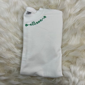 May include: White sweatshirt with green embroidered shamrocks and the name "ellison" on the front.