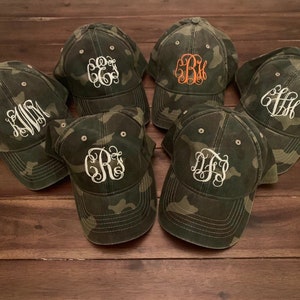 May include: Six camouflage baseball caps with different embroidered white and orange initials.