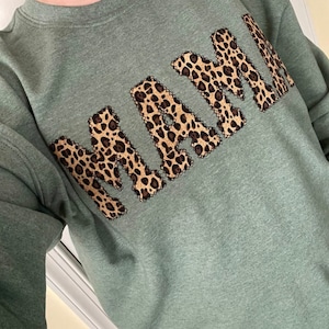 May include: A green sweatshirt with the word "MAMA" in a leopard print design.