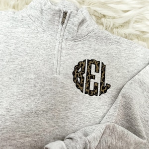 May include: A gray sweatshirt with a quarter-zip closure and a leopard print monogram "BEL" on the front.