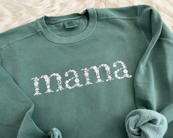 Op de afbeelding: Een groen sweatshirt met het woord "mama" geborduurd in witte bloemenletters.