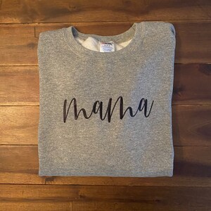 Puede incluir: Sudadera gris con la palabra "mama" escrita en letras cursivas negras.