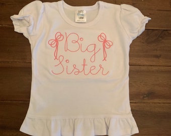 May include: White baby t-shirt with a pink embroidered design that says "Big Sister" with pink bows on either side of the word "Big".