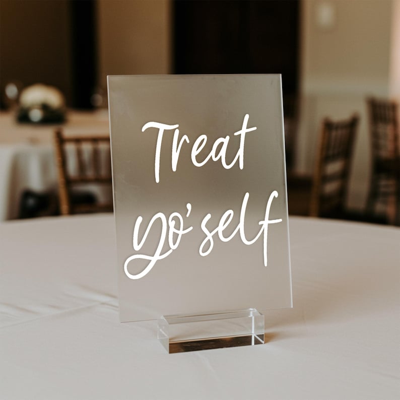 K&ouml;nnte beinhalten: Ein klares Acrylschild mit einer wei&szlig;en Aufschrift, die "Treat yo' self" lautet, auf einem klaren Acrylst&auml;nder.
