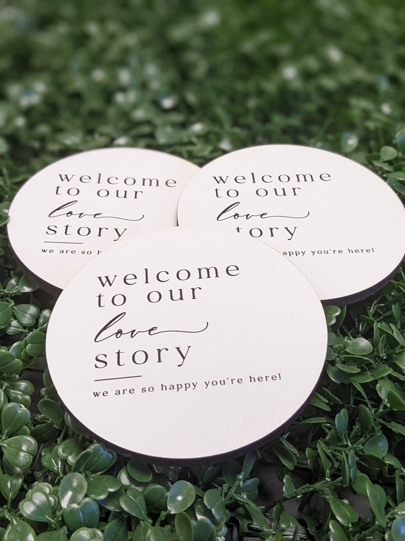 May include: Three round white signs with black text that reads "Welcome to our love story" and "We are so happy you're here!"