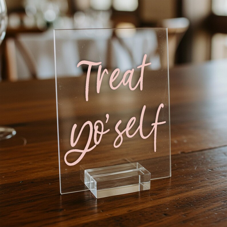 K&ouml;nnte beinhalten: Ein klares Acrylschild mit einer pinkfarbenen handgeschriebenen Nachricht, die "Treat yo' self" lautet. Das Schild steht auf einem klaren Acrylst&auml;nder.