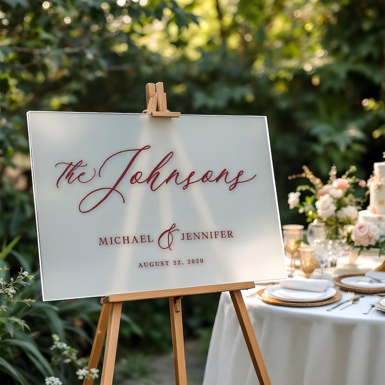 以下が含まれることがあります： 「The Johnsons, Michael & Jennifer, August 22, 2020」という文字が、赤ワイン色の文字で書かれた、フロスト加工されたガラス製の結婚式用看板です。