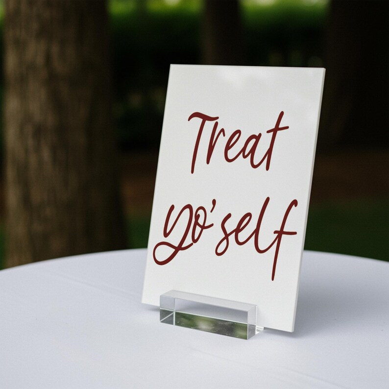 K&ouml;nnte beinhalten: Ein wei&szlig;es Schild mit einem klaren Acrylst&auml;nder. Das Schild tr&auml;gt die Aufschrift "Treat yo' self" in roten Kursivbuchstaben.