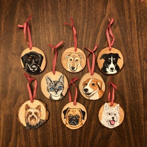 May include: Eight wooden ornaments with painted portraits of dogs and a cat. Each ornament has a red and white checkered ribbon attached.