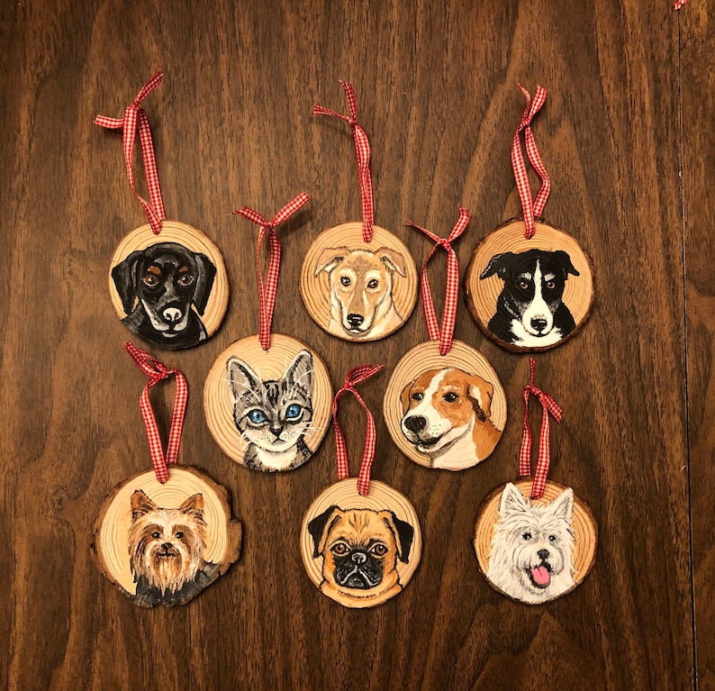 May include: Eight wooden ornaments with painted portraits of dogs and a cat. Each ornament has a red and white checkered ribbon attached.