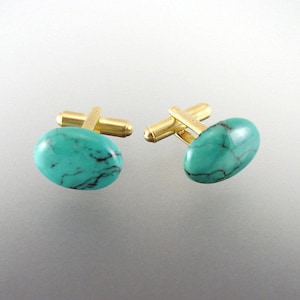 May include: A pair of gold cufflinks with oval turquoise stones. The stones have a marbled pattern of black and turquoise.