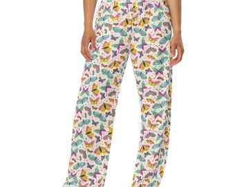 Puede incluir: Pantalones de pierna ancha con estampado de mariposas coloridas sobre fondo blanco. Las mariposas son amarillas, moradas, azules y verdes. Los pantalones se combinan con un top corto blanco y zapatillas blancas.