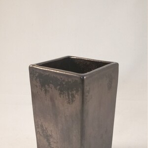 May include: A square black ceramic planter with a distressed finish. The planter has a rough, textured surface.