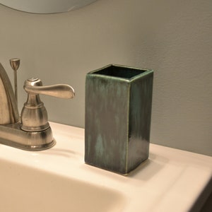 May include: A white porcelain bathroom sink with a silver faucet and two green ceramic containers. One container is a soap dispenser and the other is a toothbrush holder.