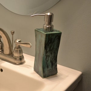 May include: A bathroom sink with a silver tap and a green ceramic soap dispenser with a silver pump.