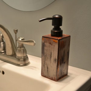 Könnte beinhalten: Ein silberner Badezimmerhahn mit einem weißen Porzellanwaschbecken und einem braunen Seifenspender mit einer schwarzen Pumpe.