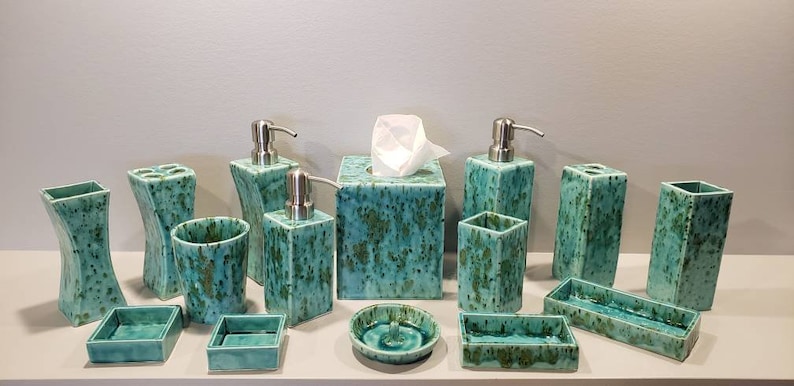 May include: A bathroom set of ceramic accessories in a teal green color with a speckled pattern. The set includes a soap dispenser, toothbrush holder, tumbler, tissue box cover, and various trays.