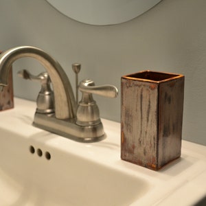 May include: A white porcelain bathroom sink with a silver faucet and a brown ceramic toothbrush holder.