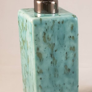 May include: A teal ceramic soap dispenser with a brushed nickel pump. The dispenser has a speckled, marbled design.