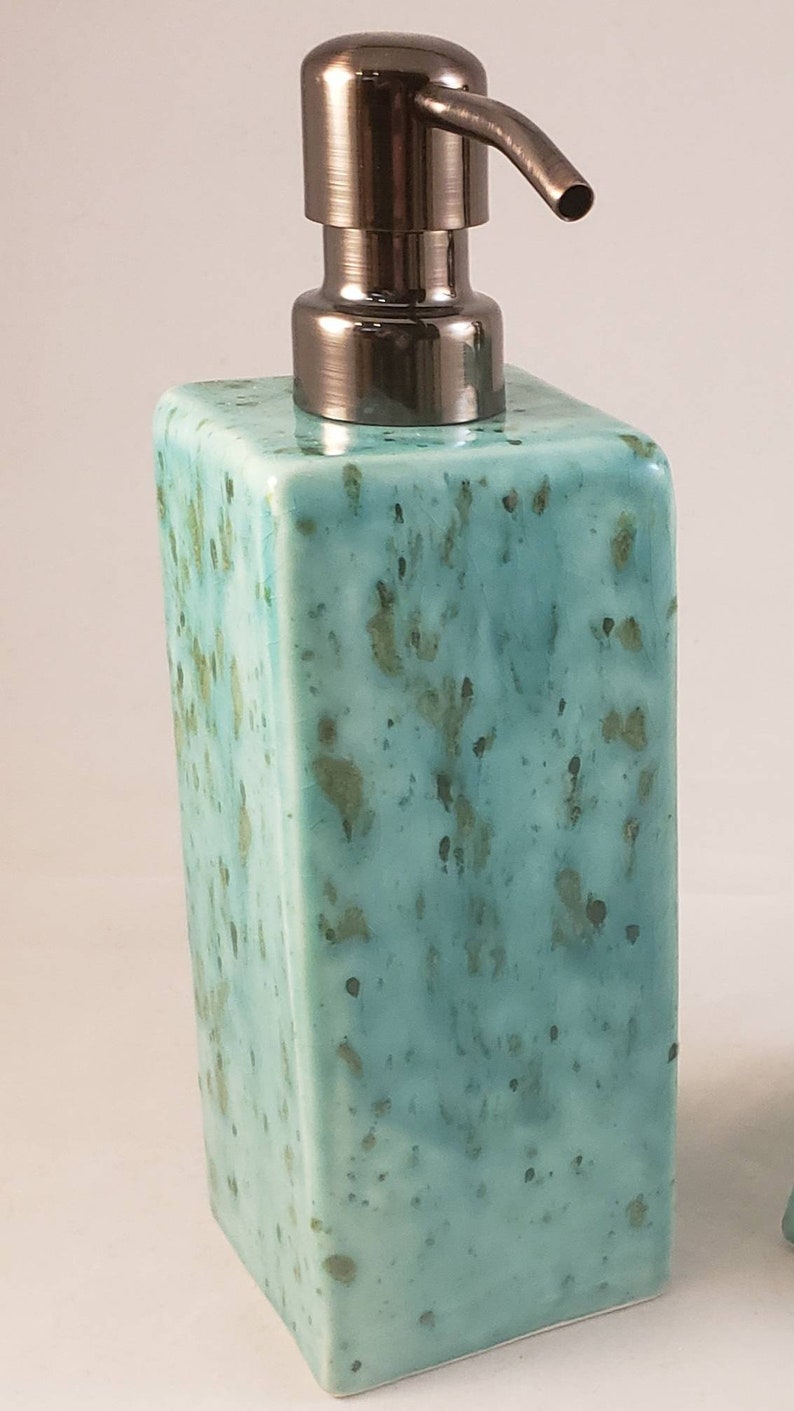 May include: A teal ceramic soap dispenser with a brushed nickel pump. The dispenser has a speckled, marbled design.