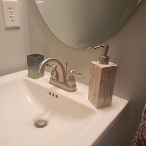 May include: A white porcelain bathroom sink with a chrome faucet and a speckled beige soap dispenser.