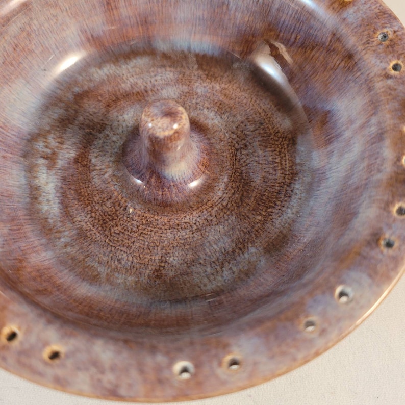 May include: A brown and white ceramic ring holder with a central knob and a ring of holes around the edge.