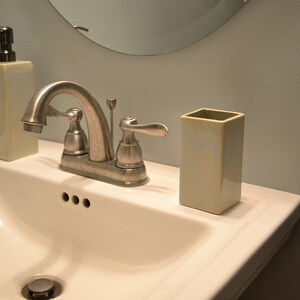 May include: A white porcelain bathroom sink with a chrome faucet and two soap dispensers. One dispenser is a rectangular bottle with a pump and the other is a cylindrical bottle with a pump.