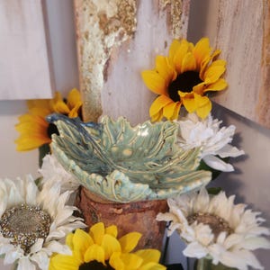 May include: A ceramic leaf-shaped dish with a green glaze and a textured surface. The dish is surrounded by sunflowers and white flowers.