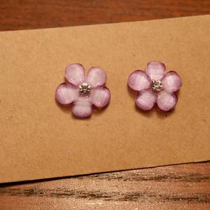 May include: A pair of purple flower earrings with a clear rhinestone in the center of each flower.