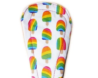 May include: A white fabric menstrual pad with a rainbow popsicle print. The pad is shaped like a teardrop and has a red stitched edge.