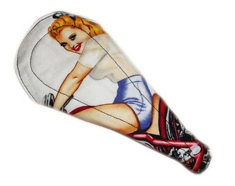 May include: A white and red motorcycle seat with a pin-up girl design. The girl is wearing a white shirt and blue shorts and is riding a motorcycle.