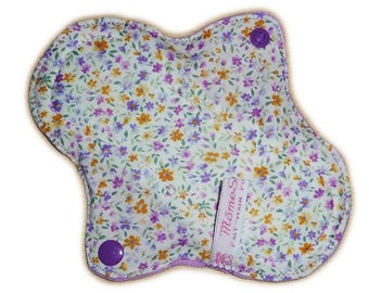 May include: A white cloth menstrual pad with a floral print in shades of purple, yellow, and orange. The pad has two purple snaps and a pink label that says "Momma's Pad" with the text "Fast - Main - Pro".