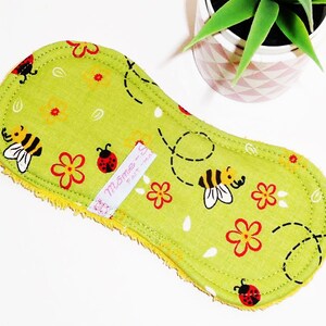May include: Green reusable cloth pad with a bee and ladybug print. The pad has a yellow border and a white label that says "M&ocirc;me -  Fait &agrave; la main".
