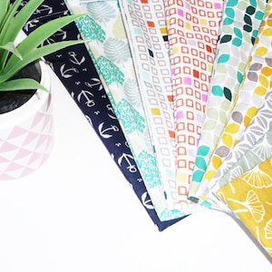 Può includere: Una collezione di 10 campioni di tessuto con vari motivi, tra cui ancore, foglie, forme geometriche e disegni floreali. I campioni sono disposti a ventaglio su una superficie bianca.