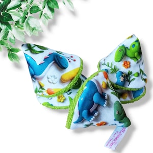 May include: Three fabric cone-shaped toys with a dinosaur theme. The cones are made of white fabric with a green trim and feature colorful dinosaur illustrations. The cones are stacked on top of each other.