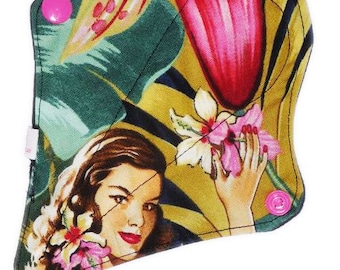 May include: A reusable cloth menstrual pad with a tropical print featuring a woman with flowers in her hair. The pad has pink poppers on the sides.