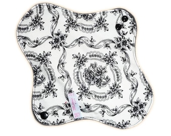 May include: A white cloth menstrual pad with a black and white floral pattern. The pad has a black snap button on each side.
