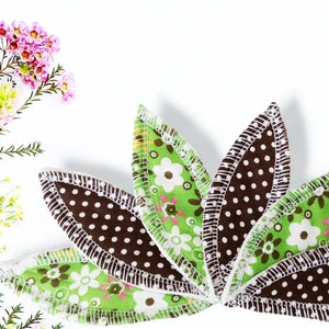Puede incluir: Diseño floral con pétalos de tela en forma de flor. Los pétalos tienen un estampado floral verde, lunares marrones y un borde cosido blanco. La imagen también incluye un ramo de flores con flores rosas y amarillas.