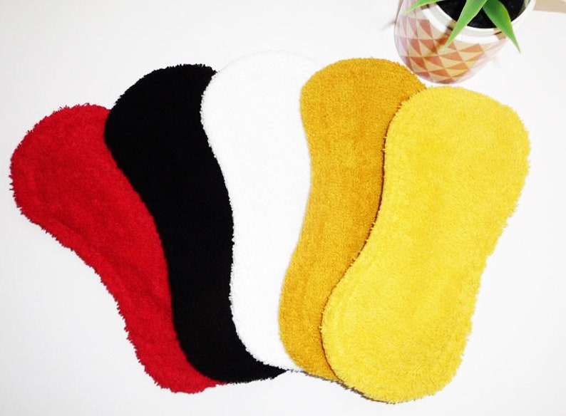 May include: Five reusable cloth menstrual pads in different colors: red, black, white, mustard yellow, and bright yellow. The pads are made of a soft, absorbent material.