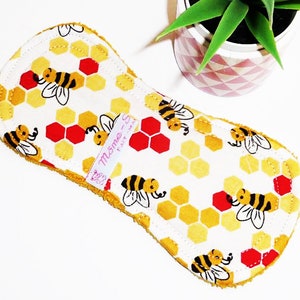 May include: A white cloth pad with a yellow honeycomb and bee pattern. The pad has a pink label that says "Mama - So Fat" on it.